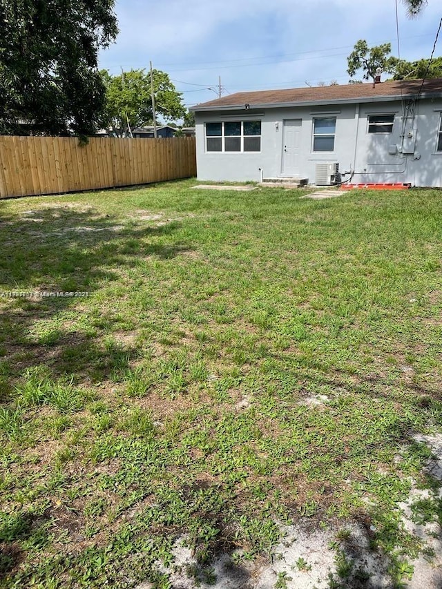 rear view of property with central AC unit and a lawn