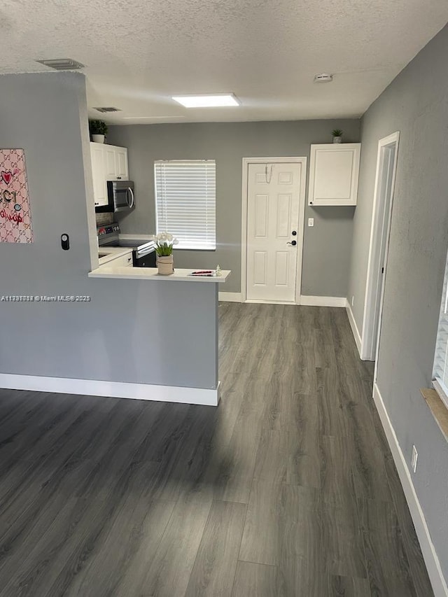 kitchen with white cabinetry, appliances with stainless steel finishes, dark hardwood / wood-style flooring, and kitchen peninsula