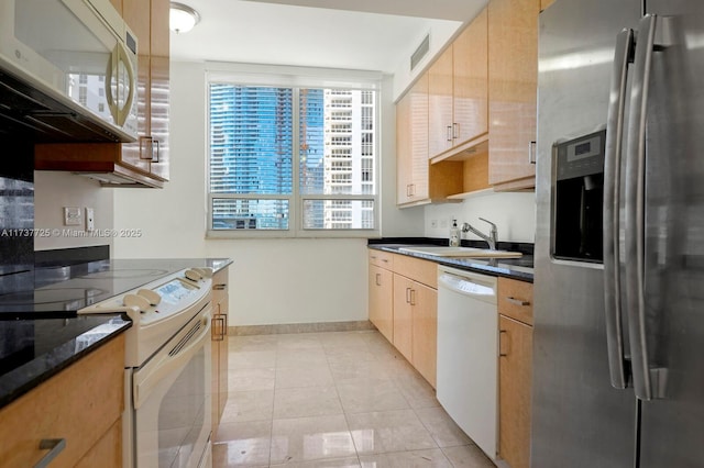 kitchen with sink, white appliances, light tile patterned floors, dark stone countertops, and hanging light fixtures