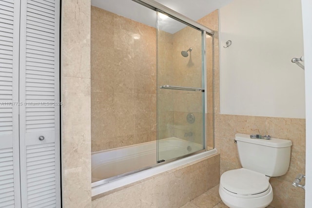 bathroom featuring tile walls, enclosed tub / shower combo, and toilet