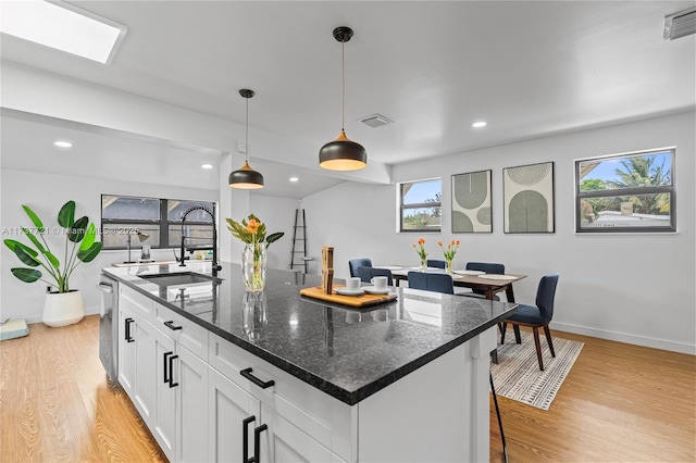 kitchen with sink, white cabinetry, decorative light fixtures, a center island with sink, and dark stone counters