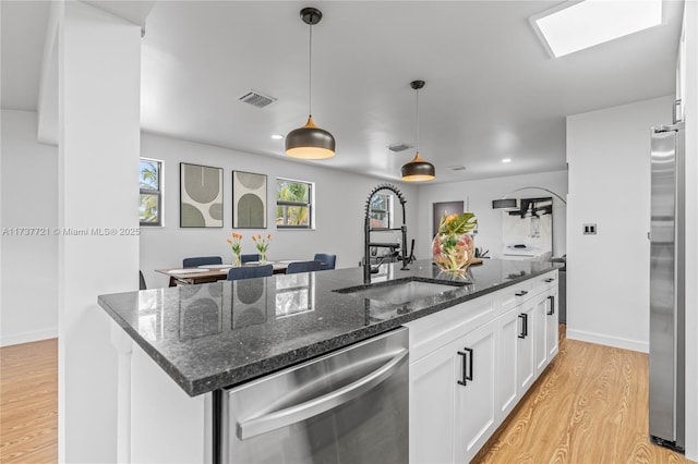 kitchen featuring appliances with stainless steel finishes, an island with sink, white cabinets, dark stone counters, and light hardwood / wood-style flooring