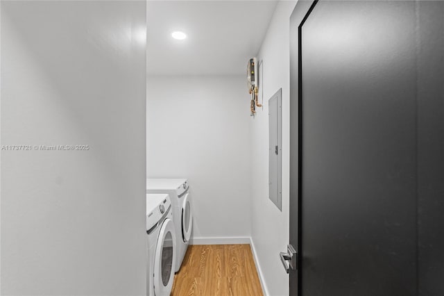 washroom featuring electric panel, washing machine and clothes dryer, and light hardwood / wood-style flooring