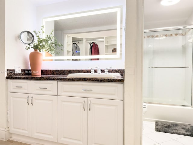 bathroom featuring tile patterned flooring, combined bath / shower with glass door, vanity, and toilet