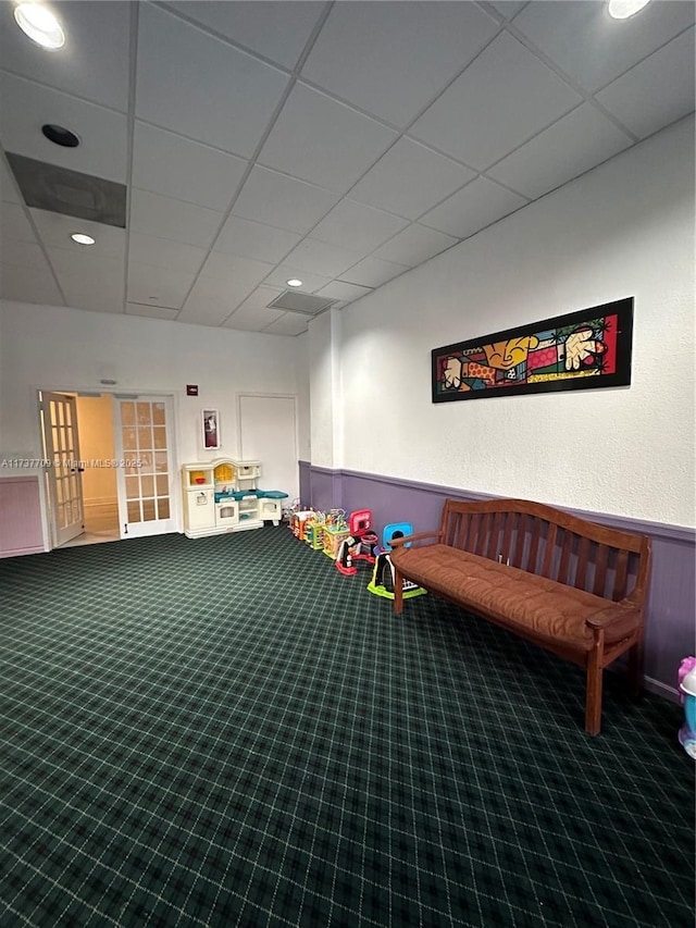 recreation room featuring a wainscoted wall, a drop ceiling, and carpet flooring