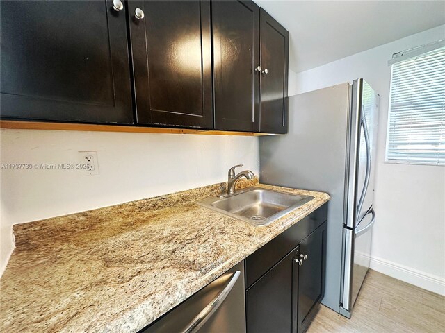 kitchen with dark brown cabinetry, sink, light hardwood / wood-style flooring, and light stone countertops