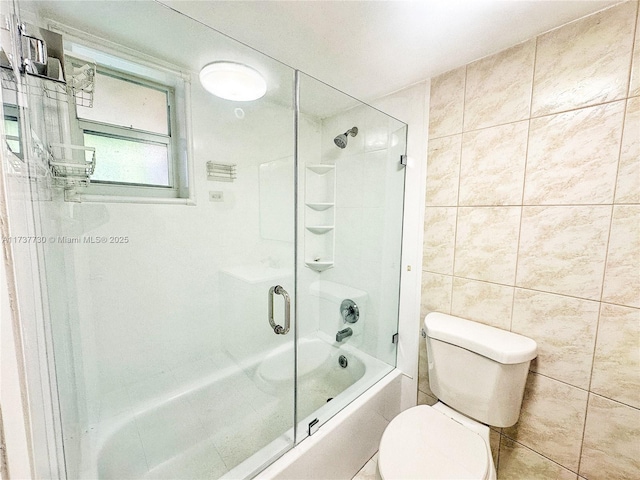 bathroom with combined bath / shower with glass door, tile walls, and toilet