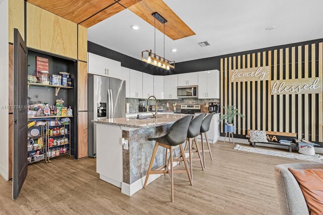 kitchen featuring sink, white cabinetry, stainless steel appliances, a center island with sink, and decorative light fixtures