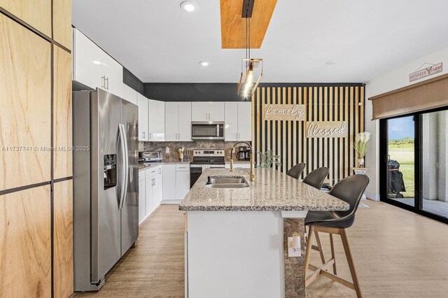 kitchen featuring sink, a breakfast bar area, white cabinetry, stainless steel refrigerator with ice dispenser, and an island with sink