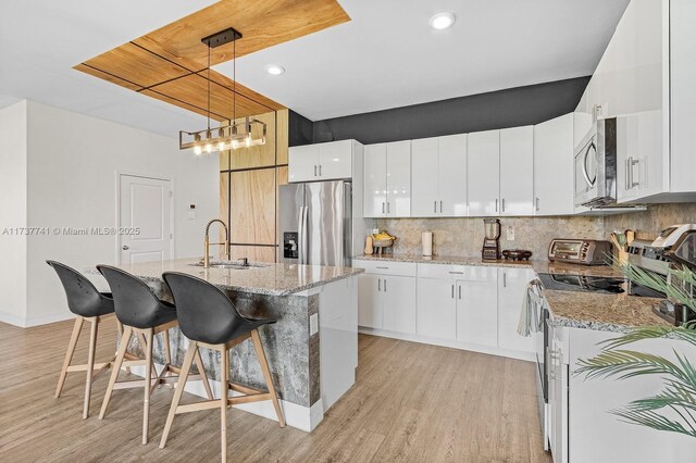 kitchen featuring pendant lighting, sink, appliances with stainless steel finishes, white cabinetry, and an island with sink