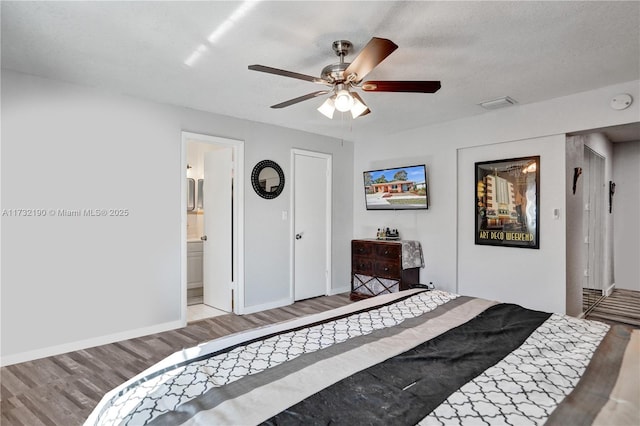 bedroom with ceiling fan, ensuite bathroom, light hardwood / wood-style flooring, and a textured ceiling