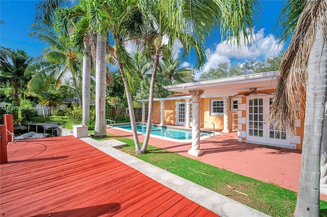 deck with french doors, a patio area, an outbuilding, ceiling fan, and a fenced in pool