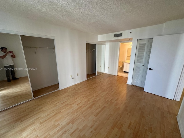 unfurnished bedroom featuring ensuite bath, two closets, a textured ceiling, and light hardwood / wood-style flooring