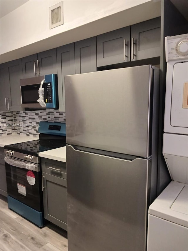 kitchen featuring appliances with stainless steel finishes, stacked washer and clothes dryer, backsplash, and light hardwood / wood-style flooring