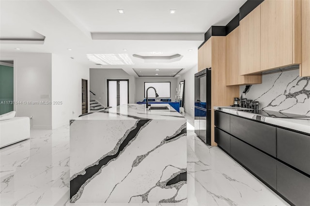 kitchen with light brown cabinetry, sink, light stone counters, a raised ceiling, and black electric cooktop