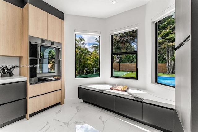 kitchen featuring a wealth of natural light, stainless steel double oven, light stone counters, and light brown cabinets