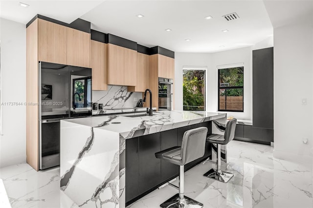 kitchen featuring sink, light stone counters, black refrigerator, a kitchen breakfast bar, and a large island