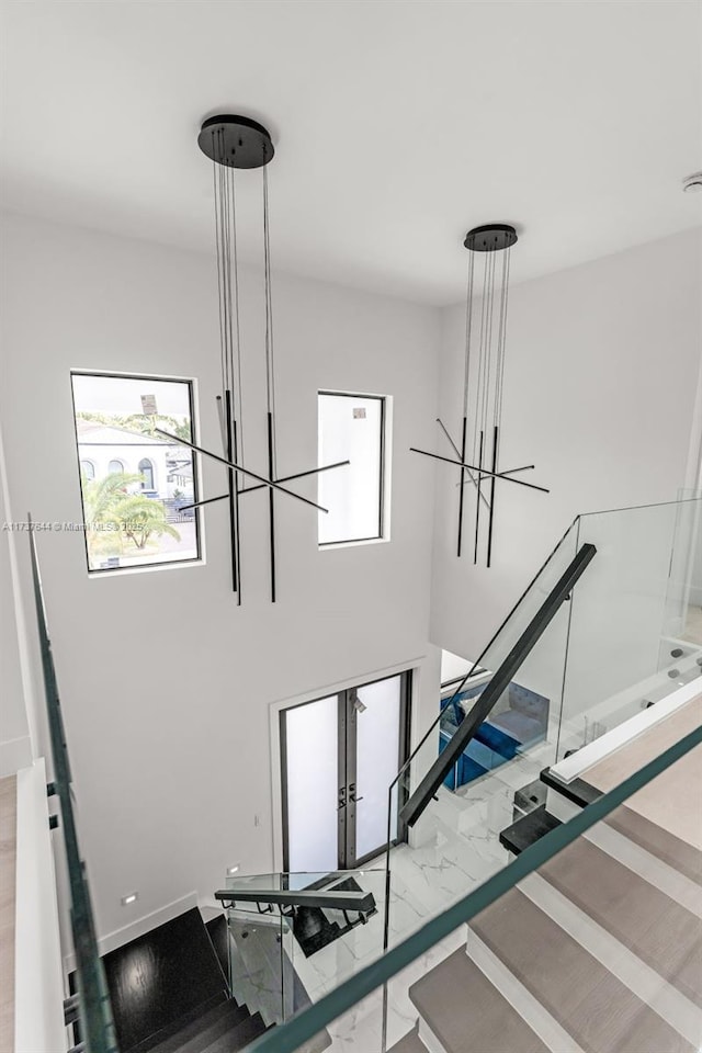 staircase featuring french doors, a notable chandelier, and a high ceiling