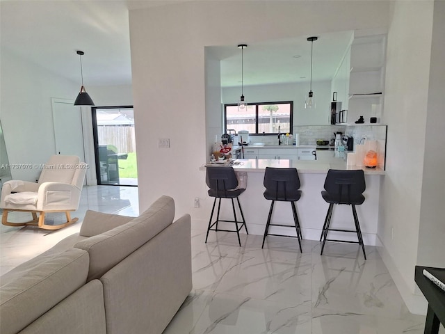 kitchen featuring white cabinetry, hanging light fixtures, decorative backsplash, and a kitchen bar