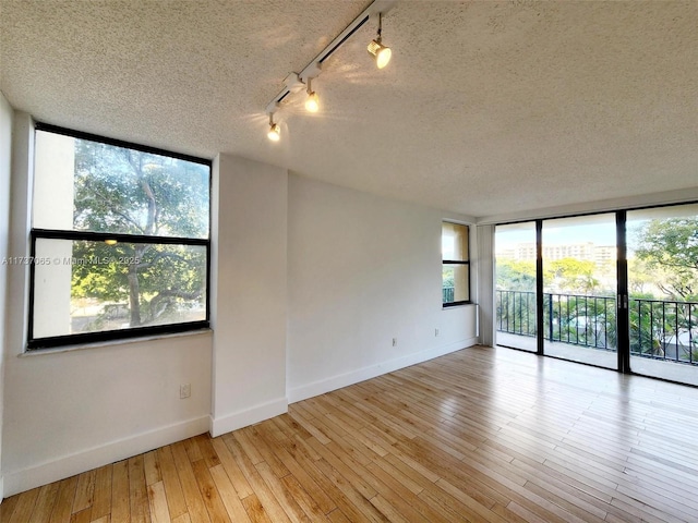 spare room featuring floor to ceiling windows, track lighting, a textured ceiling, and light hardwood / wood-style flooring