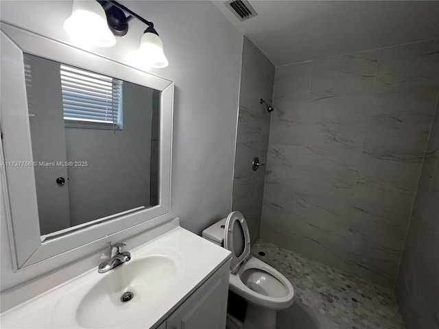 bathroom with tiled shower, vanity, and toilet