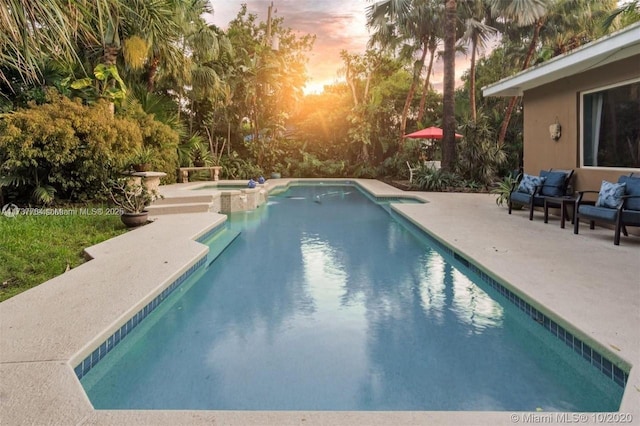 pool at dusk with a patio and an in ground hot tub