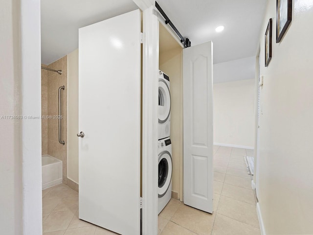 washroom featuring stacked washer and clothes dryer, light tile patterned floors, a barn door, laundry area, and baseboards