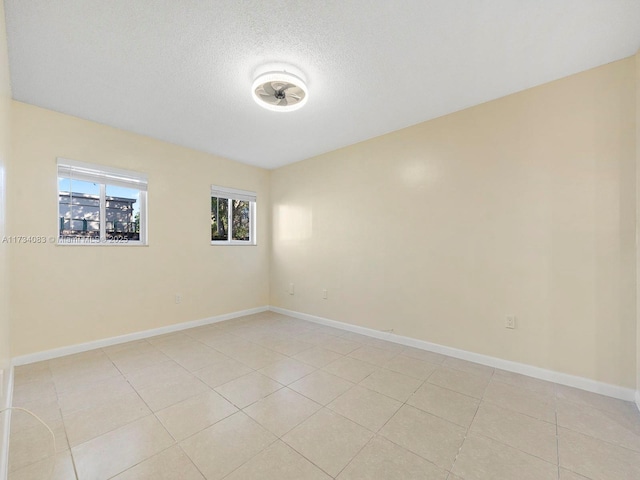 unfurnished room with a textured ceiling, light tile patterned flooring, and baseboards