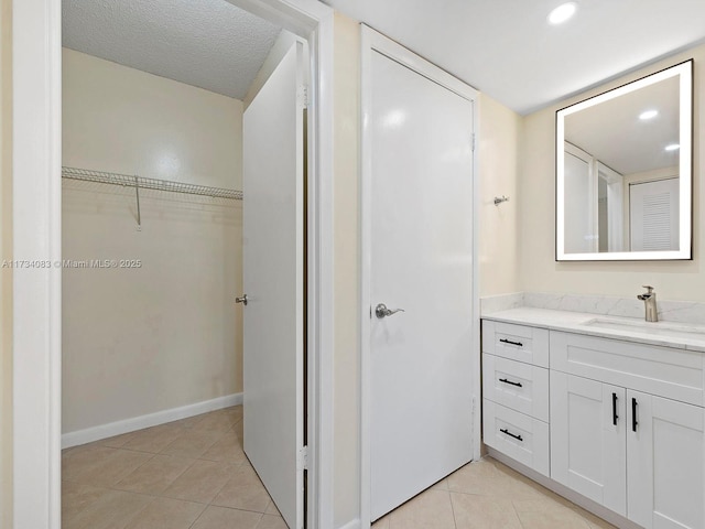 bathroom with baseboards, tile patterned flooring, a walk in closet, a textured ceiling, and vanity