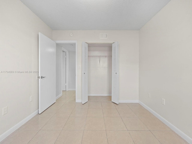 unfurnished bedroom with light tile patterned floors, baseboards, visible vents, a textured ceiling, and a closet