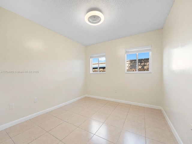 empty room with baseboards, a textured ceiling, and light tile patterned flooring