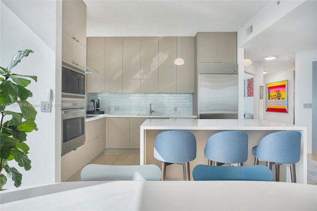 kitchen featuring sink, a breakfast bar area, gray cabinets, backsplash, and built in appliances