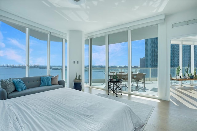 bedroom with a water view, a wall of windows, hardwood / wood-style floors, and access to outside