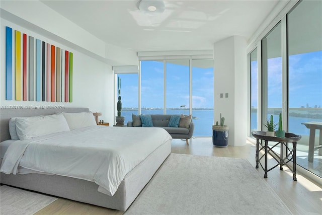 bedroom with expansive windows, a water view, access to exterior, and light hardwood / wood-style floors