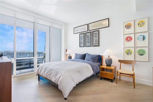 bedroom with a wall of windows and light hardwood / wood-style floors