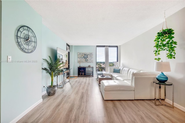 living area featuring a wall of windows, baseboards, a textured ceiling, and light wood finished floors