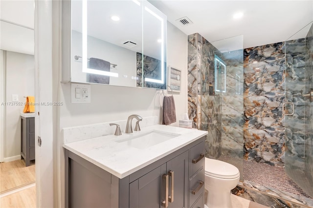 bathroom featuring tiled shower, vanity, toilet, and wood-type flooring