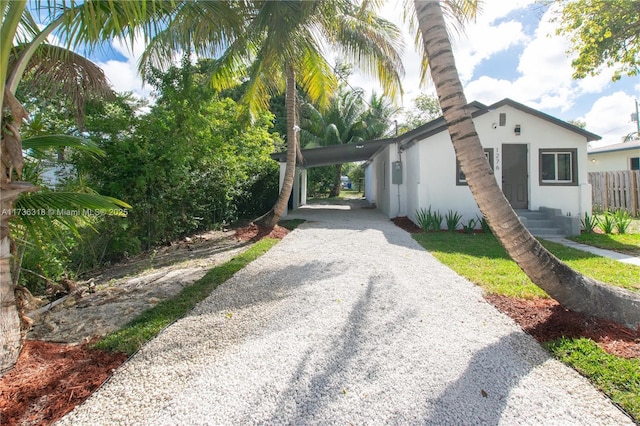 view of property exterior with a carport, stucco siding, gravel driveway, and fence