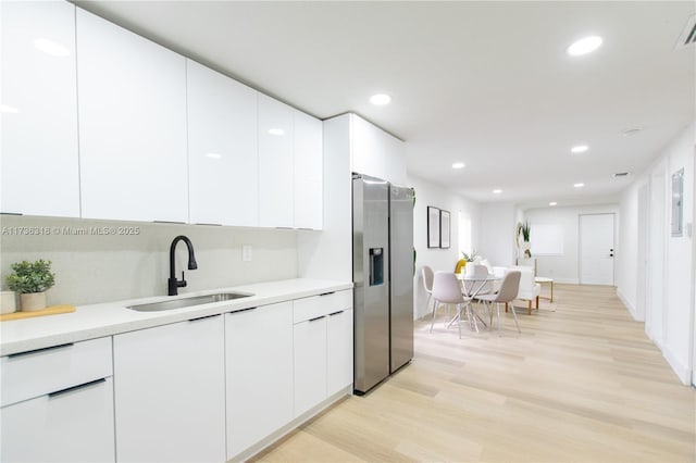 kitchen with white cabinetry, sink, stainless steel fridge, and light wood-type flooring