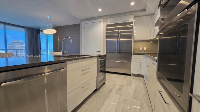 kitchen with stainless steel appliances, white cabinetry, sink, and decorative light fixtures