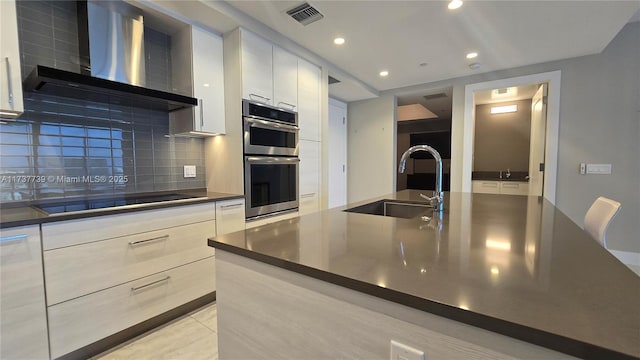 kitchen featuring wall chimney exhaust hood, sink, black electric cooktop, stainless steel double oven, and backsplash