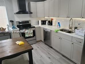 kitchen featuring wall chimney range hood, light hardwood / wood-style flooring, stainless steel appliances, and sink