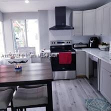 kitchen featuring electric stove, white cabinets, light hardwood / wood-style flooring, and wall chimney exhaust hood