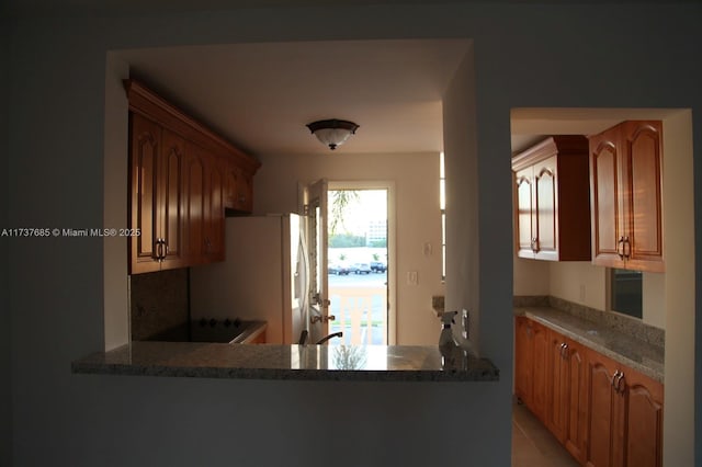 kitchen with stone countertops, kitchen peninsula, and white fridge