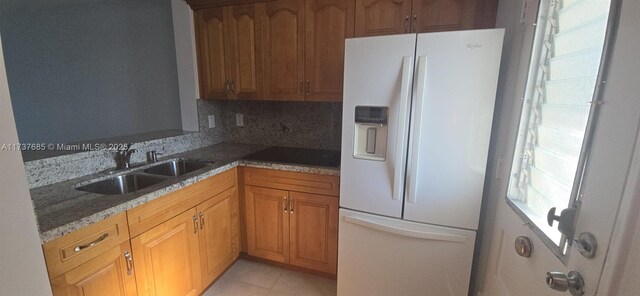 kitchen featuring sink, light tile patterned floors, white fridge with ice dispenser, dark stone counters, and backsplash