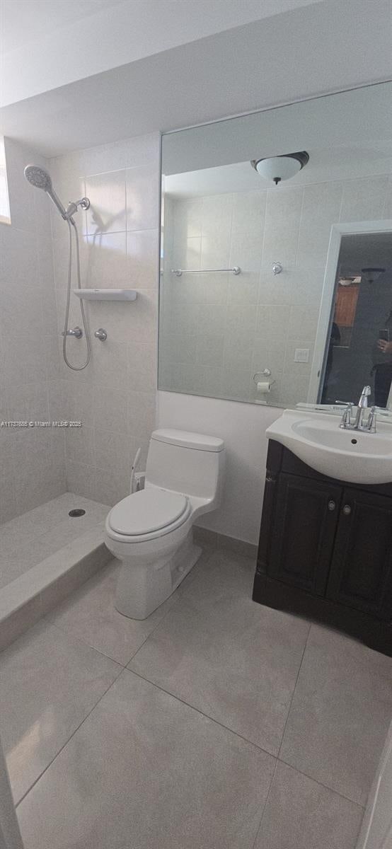 bathroom featuring vanity, tile patterned flooring, toilet, and tiled shower