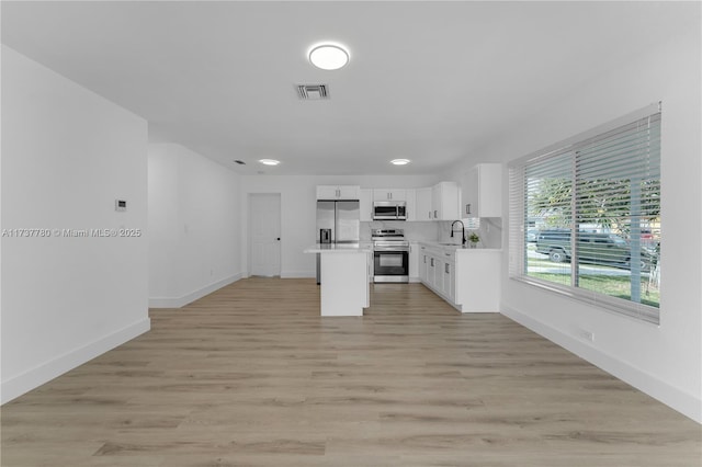 kitchen with sink, light hardwood / wood-style flooring, a kitchen island, stainless steel appliances, and white cabinets