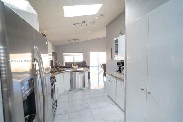 kitchen featuring sink, white cabinetry, stainless steel appliances, vaulted ceiling with skylight, and light stone countertops