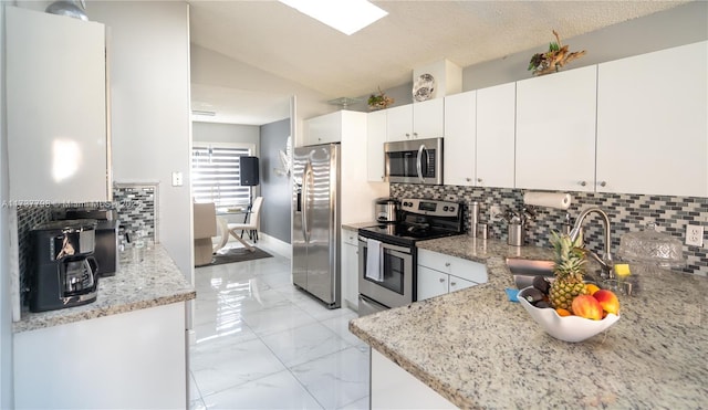 kitchen featuring lofted ceiling, sink, white cabinetry, appliances with stainless steel finishes, and light stone countertops