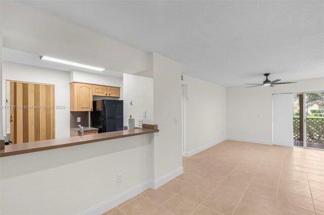 kitchen with light tile patterned floors, ceiling fan, kitchen peninsula, black fridge, and light brown cabinets